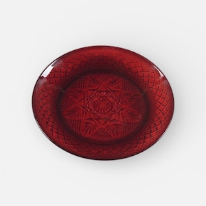 May include: A ruby red glass plate with a detailed starburst pattern in the center. The plate has a diamond-shaped textured pattern around the rim. The plate is circular and sits on a white background.