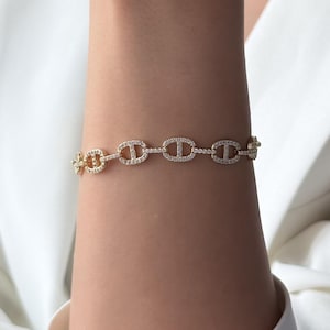 May include: A gold-toned chain bracelet featuring a series of oval-shaped links, each embedded with small, clear, sparkling stones. The bracelet has a repeating pattern of these pavé-set links connected by smaller, plain gold-toned circular rings.