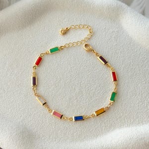 Puede incluir: Pulsera dorada con detalles rectangulares de esmalte colorido. La pulsera tiene una cadena delicada y un cierre de mosquetón. Los colores del esmalte incluyen rojo, verde, azul, amarillo, rosa y morado. Una joya elegante.
