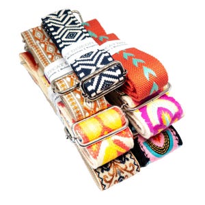 May include: A collection of adjustable bag straps featuring various woven patterns in navy blue, orange, yellow, pink, and cream. Each strap includes silver-toned metal hardware and a white paper label with the text LIPCAT DESIGN visible.