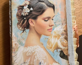 Puede incluir: Un diario hecho a mano con una cubierta de estilo vintage que presenta un retrato de una mujer con flores en el pelo. La cubierta está bordeada con una tela azul claro y un ribete con volantes. Las páginas del diario son visibles.