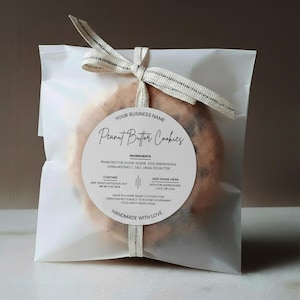 May include: A white cellophane bag tied with a cream ribbon, containing peanut butter cookies. A round label reads "Peanut Butter Cookies" with ingredient details and "Handmade with Love."