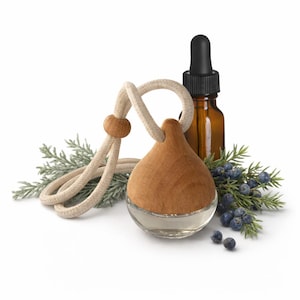 May include: A wooden and glass essential oil diffuser with a cream-colored rope and wooden bead. A small amber glass bottle with a black dropper is behind the diffuser. Green sprigs and blue berries are arranged around the diffuser.