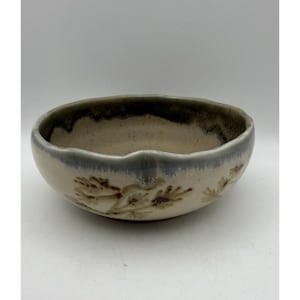 May include: A ceramic bowl with a cream-colored interior and a dark gray rim. The exterior features a light gray band and brown floral designs. The bowl has a slightly irregular, wavy edge.