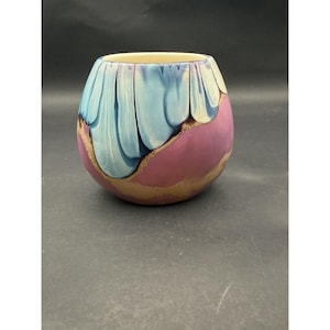 May include: A rounded ceramic vase featuring a smooth, glossy finish with a distinct colour-blocked design. The upper portion displays vertical, petal-like streaks of light blue and dark blue, while the lower section is a solid, muted mauve-pink.