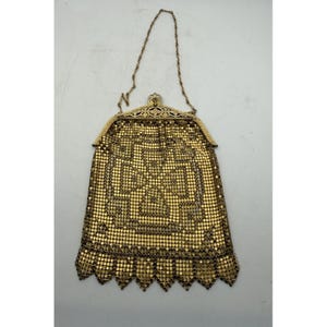 May include: A gold-toned metal mesh handbag featuring a geometric pattern and a scalloped bottom edge. The bag includes an ornate, engraved metal frame with a top clasp and a thin, delicate chain handle for carrying the accessory by hand.