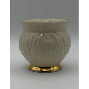 May include: A cream-coloured ceramic vessel featuring a bulbous body with an embossed leaf pattern. The top rim has a subtle vertical ribbed texture, while the base is finished with a smooth, reflective gold-toned band around the bottom edge.