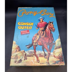 Könnte beinhalten: Ein rechteckiger Pappkarton für ein Pony Boy Cowboy-Outfit. Die blaue Schachtel zeigt eine Vintage-Illustration einer Person in rotem Hemd und Cowboyhut auf einem braunen Pferd. Der Text umfasst Pony Boy, Cowboy Outfit und Nationally Advertised.