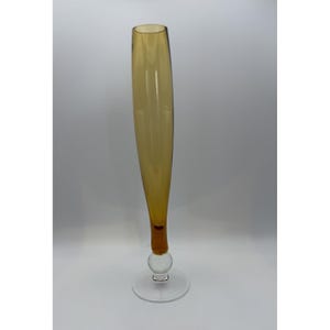 May include: A tall, slender amber glass vase. The vase has a long, cylindrical shape that tapers slightly towards the top. It features a clear, round base and a spherical accent near the bottom. The vase is approximately 30 cm tall.
