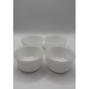 May include: Four small, white, round bowls are grouped together. The bowls have a simple, minimalist design with a slightly flared rim. The bowls are made of a solid, opaque material, and are suitable for serving small portions.