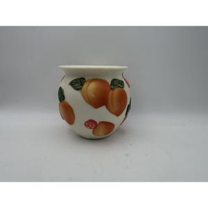 May include: A round, off-white ceramic planter featuring a hand-painted pattern of orange peaches with green leaves and small pink flowers. The vessel has a wide, slightly flared rim and a smooth, curved body that tapers toward the base.