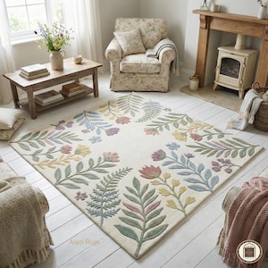 May include: Cream-coloured rectangular rug with a floral design. The rug features a border of colourful flowers and leaves in shades of pink, blue, yellow, and green. The rug is placed in a living room setting with a floral armchair and wooden furniture.
