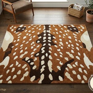 May include: A rectangular brown area rug with a deer-like pattern. The rug features a brown background with white and dark brown spots and shapes. The rug is placed on a hardwood floor.