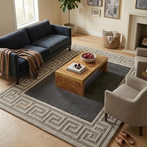 May include: A living room scene featuring a navy blue sofa, two beige armchairs, and a wooden coffee table. A large gray rug with a Greek key border sits on the hardwood floor. Artwork hangs on the wall.