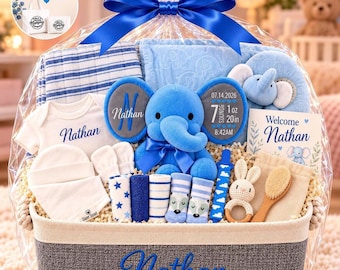 Op de afbeelding: Een babycadeaumand verpakt in doorzichtig plastic met een blauwe strik, met een blauwe pluche olifant, een wit rompertje, een gestreepte deken, sokjes, een houten borstel, een gehaakte rammelaar en een kaartje, gepersonaliseerd met de naam Nathan.