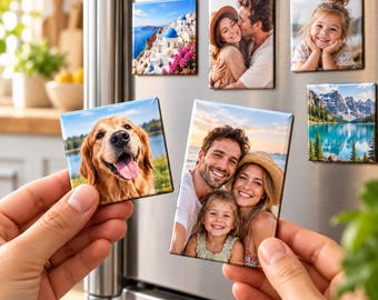 May include: A collection of rectangular photo magnets featuring various images including a coastal town, a couple, a child, a golden retriever, and a mountain lake. The magnets are displayed on a stainless steel refrigerator surface.