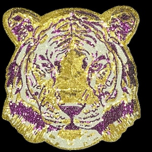 May include: A decorative tiger head patch, featuring gold, cream, and purple sequins. The tiger's face is detailed with gold sequins, with purple stripes and accents. This patch is likely for embellishing clothing or accessories.