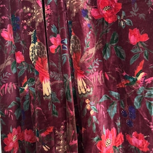 Könnte beinhalten: Burgunderfarbener Samtstoff mit einem Blumen- und Vogelmuster. Das Design zeigt große rote und rosa Blüten, grüne Blätter und farbenfrohe Vögel. Der Stoff hat eine weiche, luxuriöse Textur und eine satte Farbpalette.