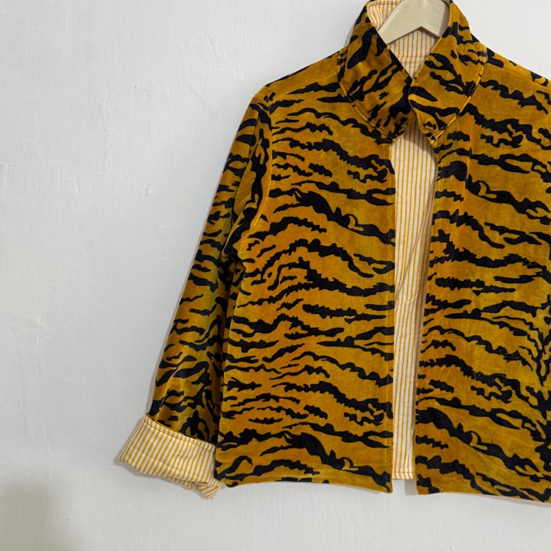 May include: A mustard yellow jacket with a black tiger stripe pattern. The jacket has a collared neckline and long sleeves with a striped cuff. The interior lining is a light yellow and white striped fabric.