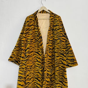 May include: A long, open-front robe with a tiger stripe pattern in black and yellow. The robe is hanging on a wooden hanger against a white background. The interior lining is yellow and white striped.