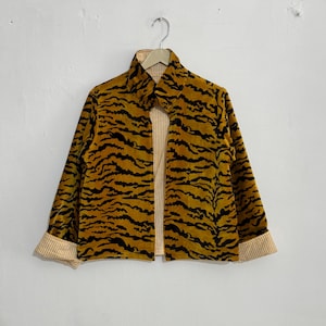 May include: A mustard yellow jacket with a black tiger stripe pattern. The jacket has a collared neckline and long sleeves with striped cuffs. The interior lining is a light yellow and white striped fabric.