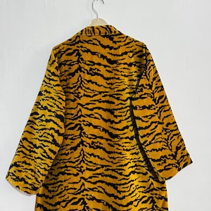 May include: A long, open-front robe with a tiger stripe pattern in shades of yellow and black. The robe is hanging on a hanger against a white wall. The sleeves are wide and three-quarter length.