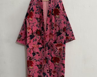 May include: A pink floral print robe with a red and navy blue design. The robe has long sleeves, two front pockets, and a striped interior. It is hanging on a wooden hanger against a white wall.