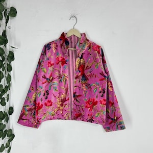 Pode incluir: Casaco rosa com padrão floral, gola alta e mangas compridas. O casaco apresenta um design vibrante de pássaros, flores e folhagem em tons de vermelho, amarelo e verde. O forro interior tem um padrão listrado.