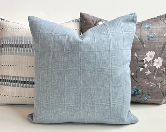 Puede incluir: Cuatro cojines decorativos con varios patrones y colores. El cojín delantero es azul claro con un patrón de cuadrícula. Otros cojines presentan un diseño geométrico blanco y azul, un estampado floral y un estampado floral marrón y blanco.