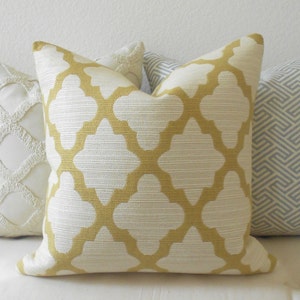 May include: A square decorative pillow with a white background and a gold quatrefoil pattern. The pillow has a textured appearance and is part of a set of pillows with different designs.