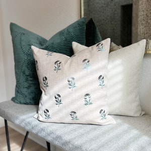 K&ouml;nnte beinhalten: Drei dekorative Kissen auf einer grauen Bank. Das mittlere Kissen ist beige mit einem floralen Muster in Schwarz und Blau. Das Kissen links ist aus dunkelgr&uuml;nem Cord. Das Kissen rechts hat ein wei&szlig;-graues Fischgr&auml;tenmuster.