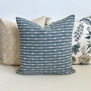 May include: Three decorative throw pillows with different patterns. The center pillow is a dark blue with white stripes and dots. The pillow on the left is a yellow with a paisley pattern. The pillow on the right is a white with a floral pattern.