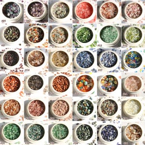 May include: A collection of small, colorful gemstone chips displayed in individual white containers. The gemstones vary in color, including shades of purple, green, red, orange, blue, and clear. Each container is labeled with a number from #01 to #36.