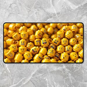 May include: A rectangular mousepad featuring a close-up of numerous yellow Lego minifigure heads with various facial expressions. The heads are scattered across the mousepad, creating a playful and engaging design.