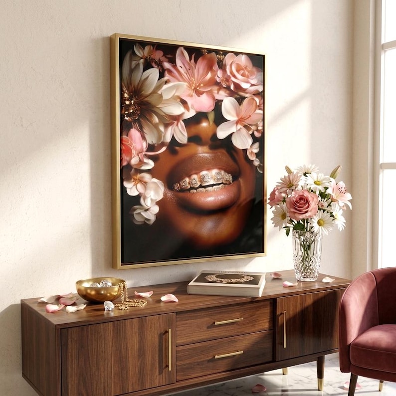 May include: A framed wall art print featuring a close-up of a person with dark skin wearing gold teeth grills, surrounded by a crown of soft pink and white flowers. The artwork is displayed in a gold frame, capturing a vibrant floral aesthetic.