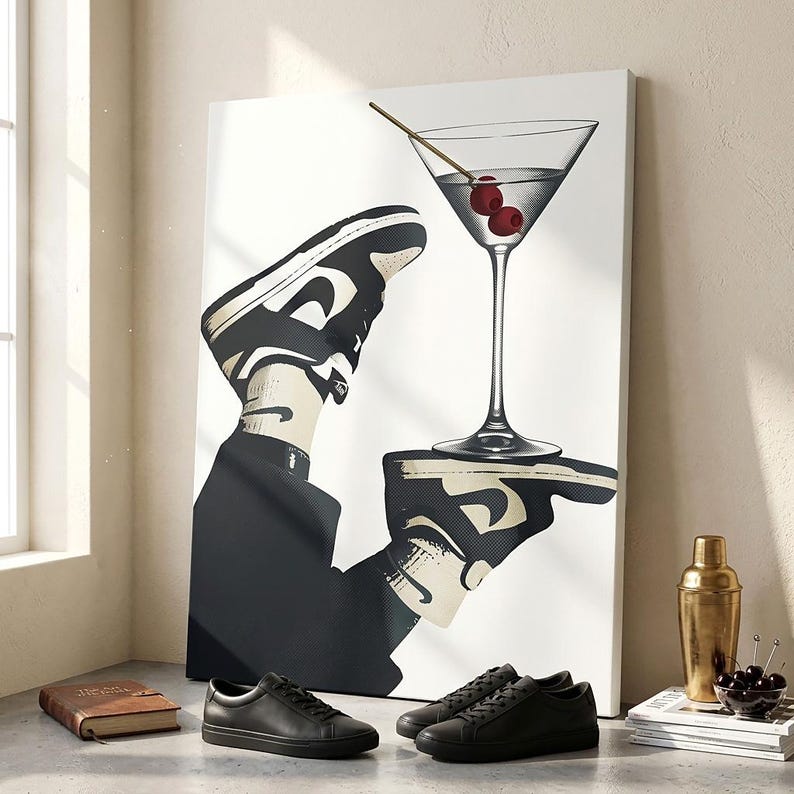 May include: A rectangular canvas print featuring a graphic illustration of a person wearing black and white sneakers, holding a martini glass with two red cherries on a toothpick. The artwork is displayed on a surface with black leather sneakers.