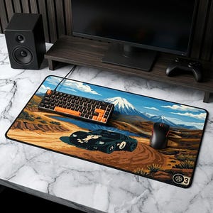 May include: A rectangular pixel art mousepad featuring a black sports car on a dirt road with a mountain backdrop. A black and orange keyboard and a red and black mouse are on the pad. The pad has a black border.