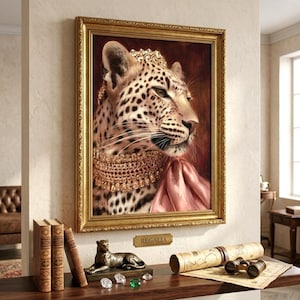 May include: A framed portrait of a leopard wearing a jeweled crown and a thick gold collar with a pink fabric drape, set in an ornate gold frame. Below the frame, a small plaque reads REGALIA, accompanied by a leopard figurine and binoculars.