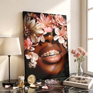 May include: A rectangular canvas print featuring a close-up of a person with dark skin wearing gold grillz on their teeth, surrounded by a crown of soft pink and white flowers. The artwork is displayed on a black marble surface with decorative items.