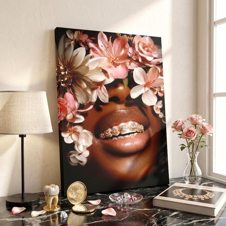 May include: A rectangular canvas print featuring a close-up of a person with dark skin wearing gold grillz on their teeth, surrounded by a crown of soft pink and white flowers. The artwork is displayed on a black marble surface with decorative items.