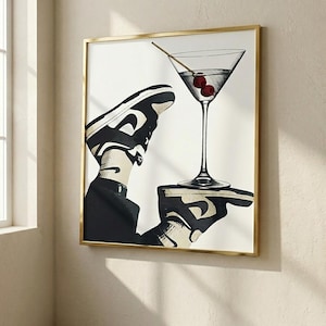May include: A framed wall art print featuring a black and white graphic illustration of a sneaker-clad foot balancing a martini glass with two red cherries on a flat palm. The artwork is encased in a thin, metallic gold-colored rectangular frame.