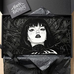May include: A black and white illustration of a woman with long black hair and dark makeup on a rectangular mousepad. The mousepad is in a black box with a "Happy Birthday" card. The design includes spiderwebs and spiders.