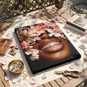May include: A rectangular canvas print featuring a close-up of a person with dark skin, full lips, and diamond-encrusted teeth grills, surrounded by soft pink and white floral blossoms against a dark background, displayed on a wooden table.