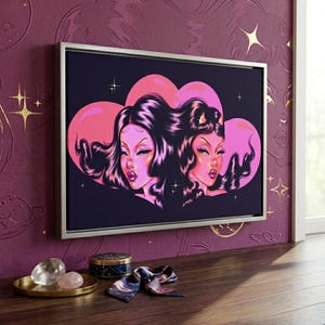 May include: A framed canvas art print featuring two stylized female figures with long, dark hair and pink skin tones. The artwork is set against a dark blue background with pink heart-shaped elements and small star accents. The frame is silver.