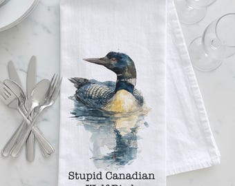 May include: White kitchen towel featuring a watercolor painting of a loon floating on water. The bird has black, blue, and yellow plumage. Text at the bottom reads "Stupid Canadian Wolf Bird."