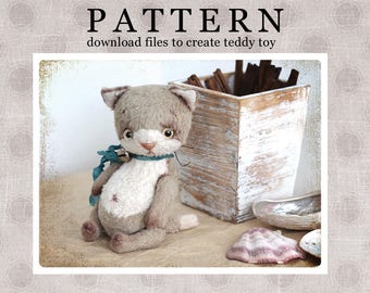 Puede incluir: Un oso de peluche gris y blanco con forma de gato con una cinta azul alrededor del cuello y una campana. El juguete está sentado sobre una superficie marrón claro con una caja de madera y conchas marinas.