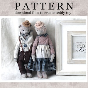 May include: Two handmade teddy bears, one wearing a brown hat and brown pants, the other wearing a pink hat and a blue and white plaid dress. The bears are standing in front of a white frame with the text "Teddy Bears B" and a cursive "B" in the frame.