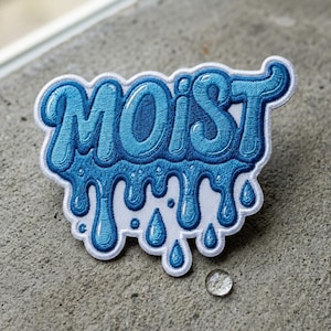 May include: A blue embroidered patch with the word "MOIST" in a stylized font. The word is dripping with water droplets, and the patch has a white border. The patch is on a gray concrete surface.