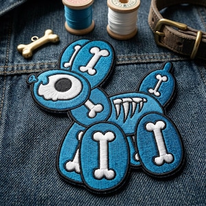 May include: A blue embroidered patch in the shape of a balloon dog, featuring white bone accents and a black outline. The patch is on a denim background, with a gold bone charm, spools of thread, and a brown dog collar.