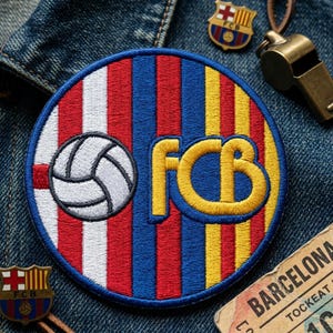 May include: A round embroidered patch with the letters "FCB" in yellow, a soccer ball, and red, blue, and yellow stripes. The patch is on a denim background, with a pin and a whistle.